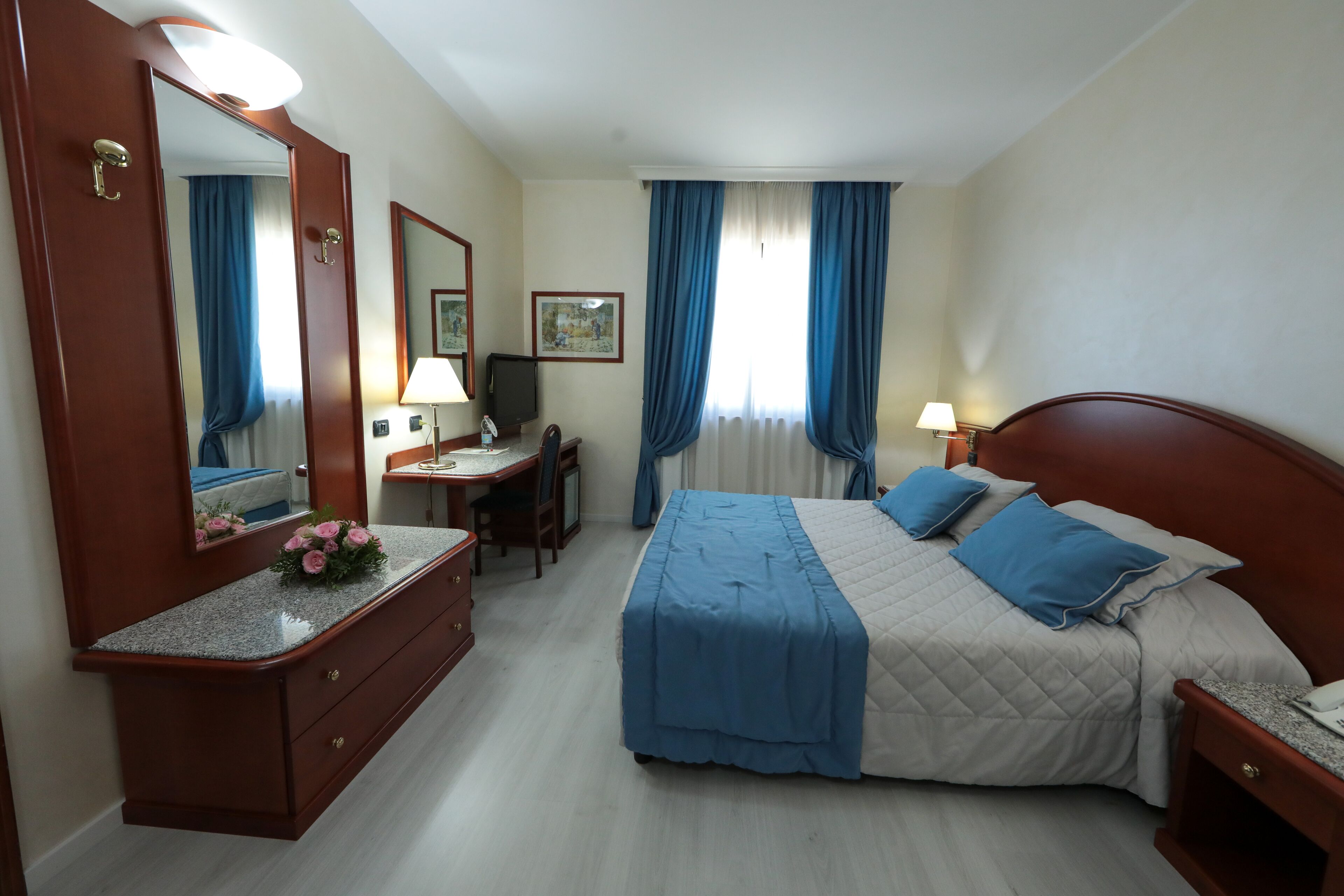 Habitación de hotel con cama, escritorio, cómoda, espejo y ventana con cortinas.