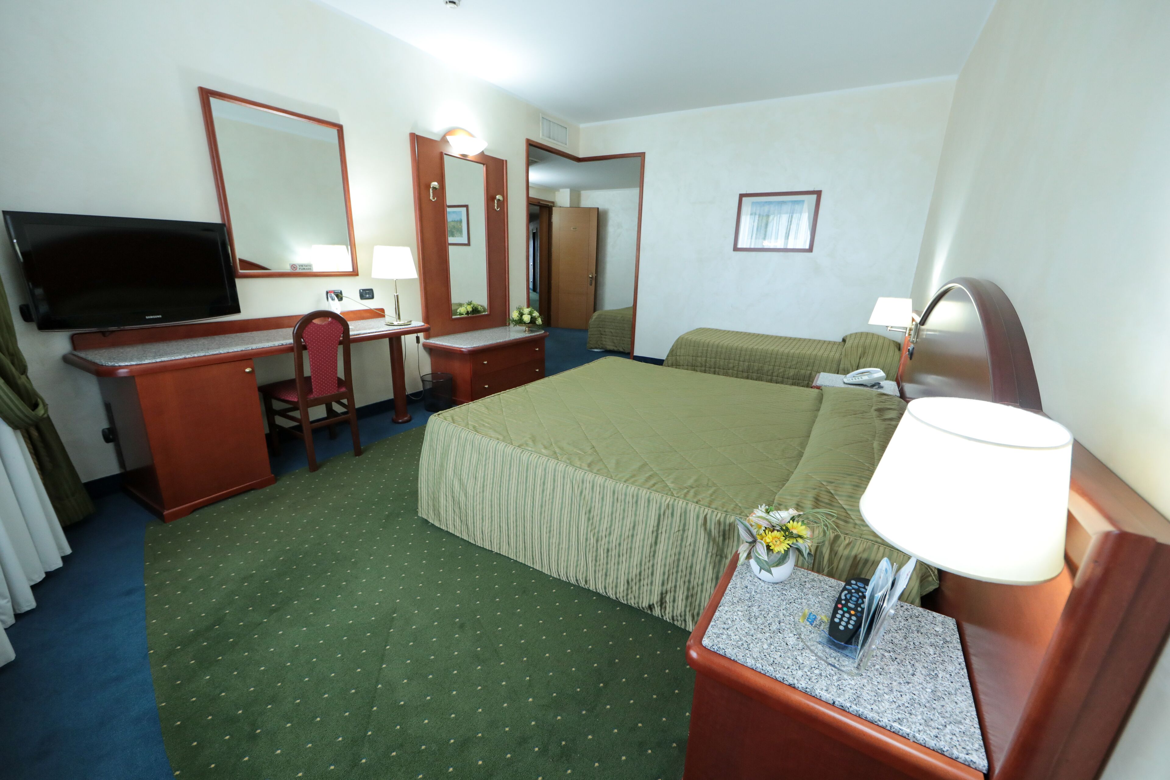 Une chambre d’hôtel comprenant un lit, un bureau avec une chaise, une télévision, un miroir et une table de chevet avec une lampe.