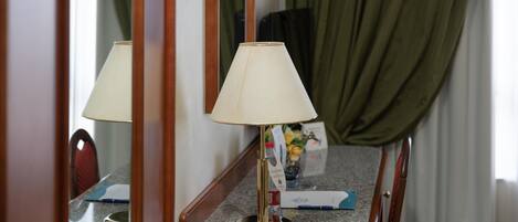 Una habitación de hotel con una silla de madera, una mesa con una lámpara y un espejo que refleja la habitación.