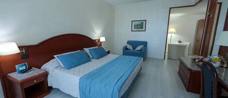 A hotel room with a bed, a desk, a chair, a nightstand, and a mirror.