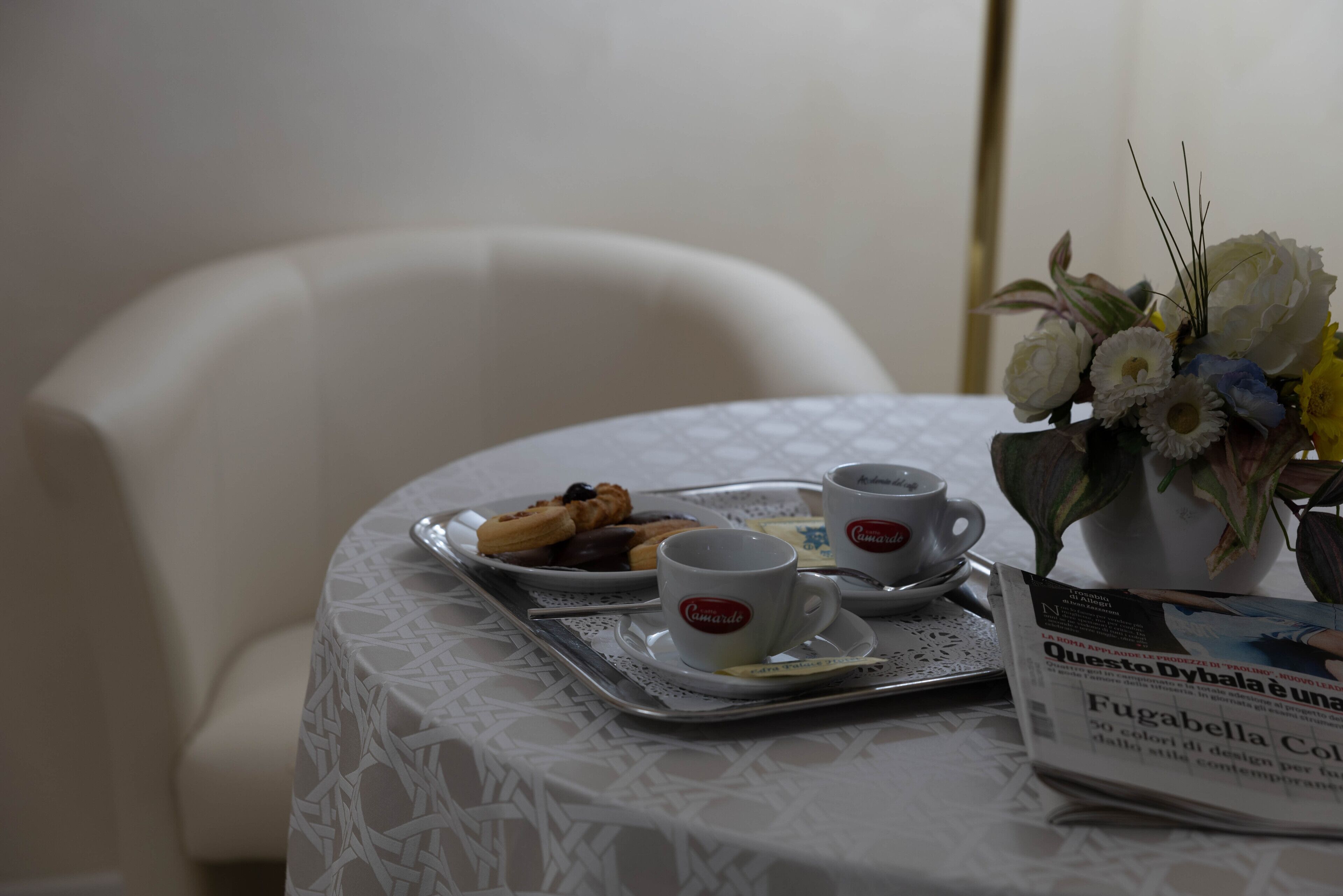 Una mesa con una bandeja de pasteles, dos tazas y un florero.