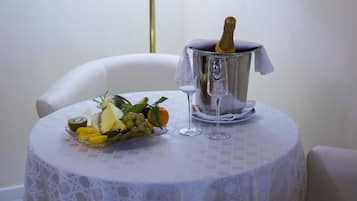 Una mesa redonda con mantel blanco, un frutero, una botella de champán en un cubo y dos copas de vino.