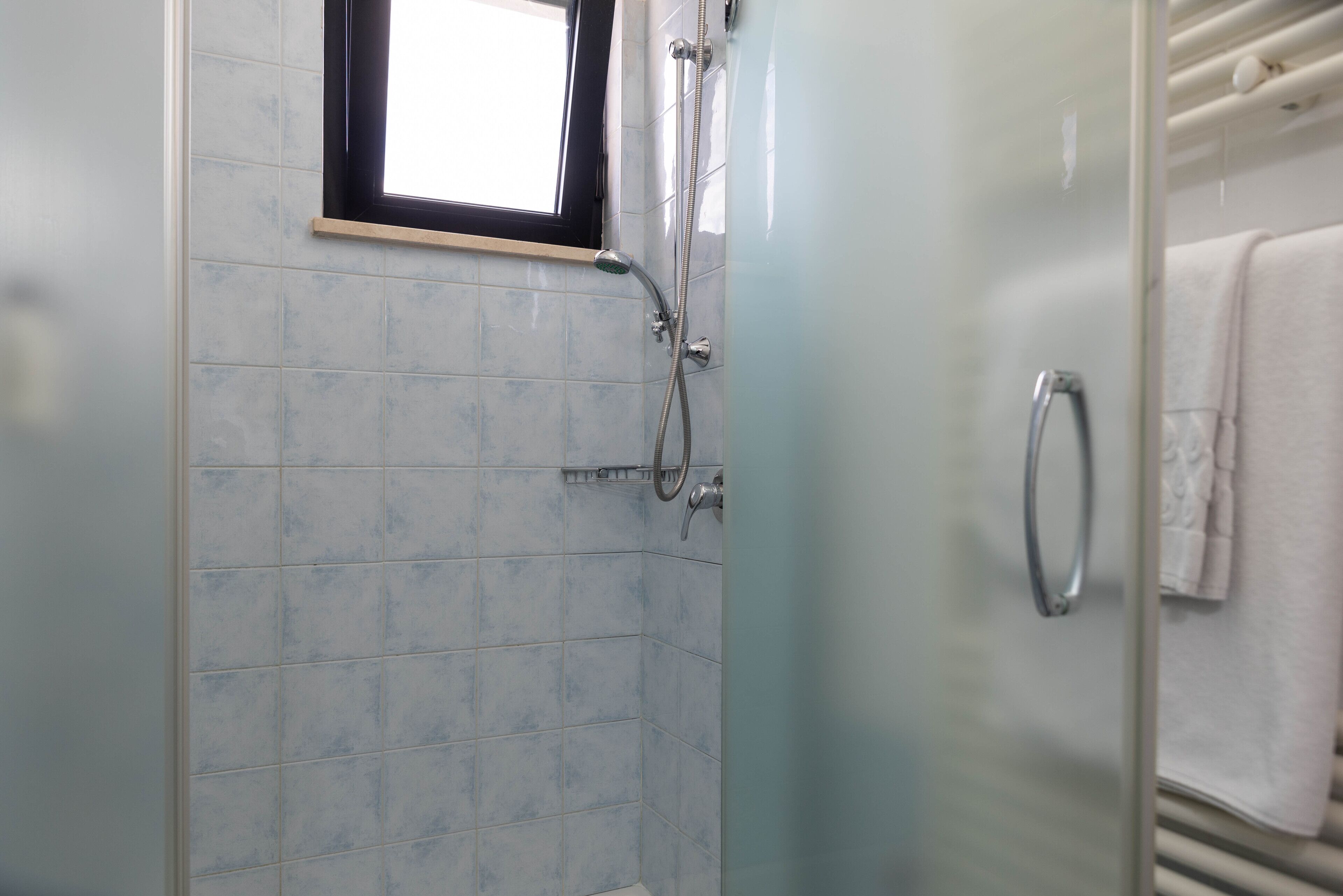 A bathroom with a glass shower enclosure, a window, and a towel rack.