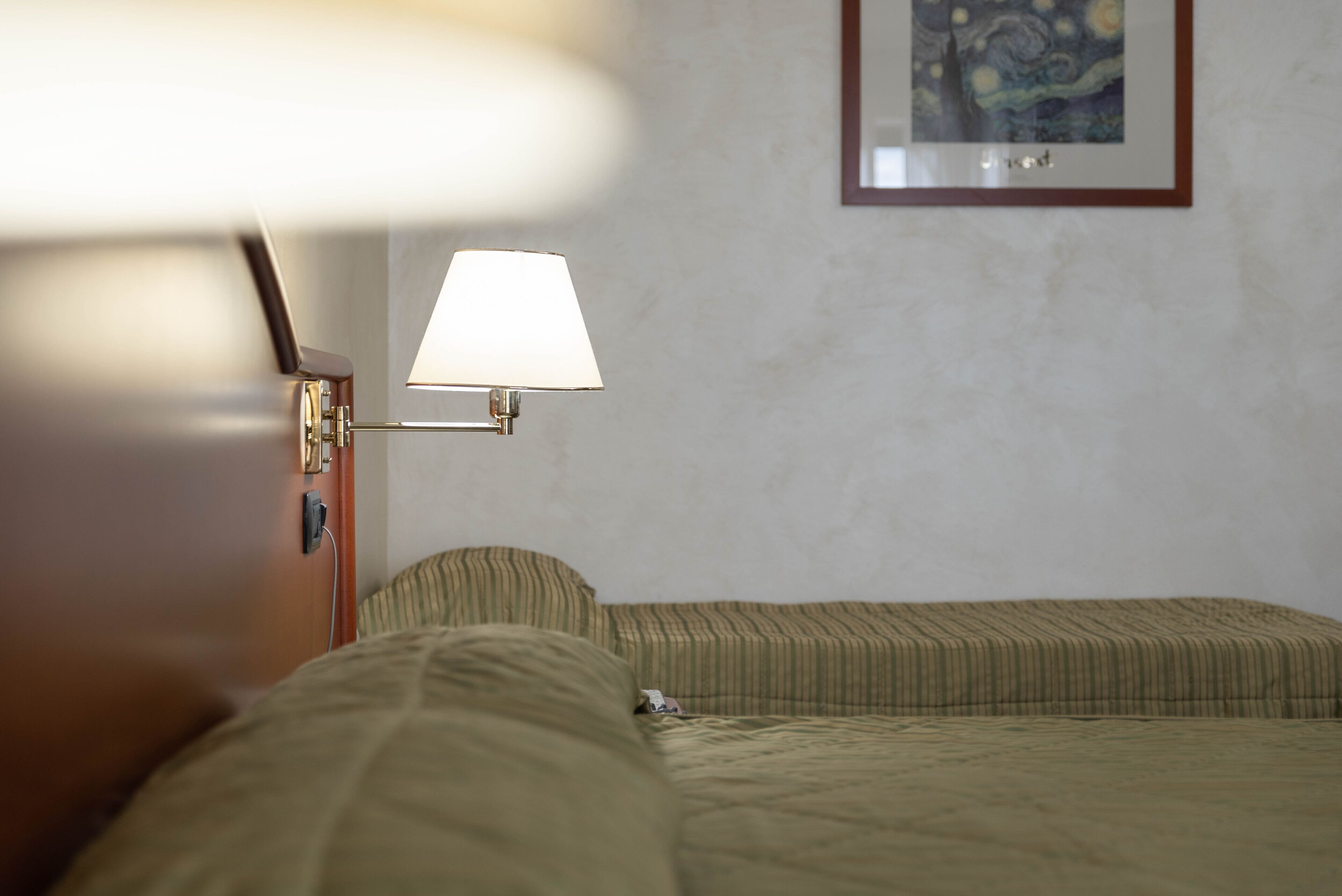A hotel room with a bed, a bedside lamp, a framed artwork on the wall, and a window with curtains.