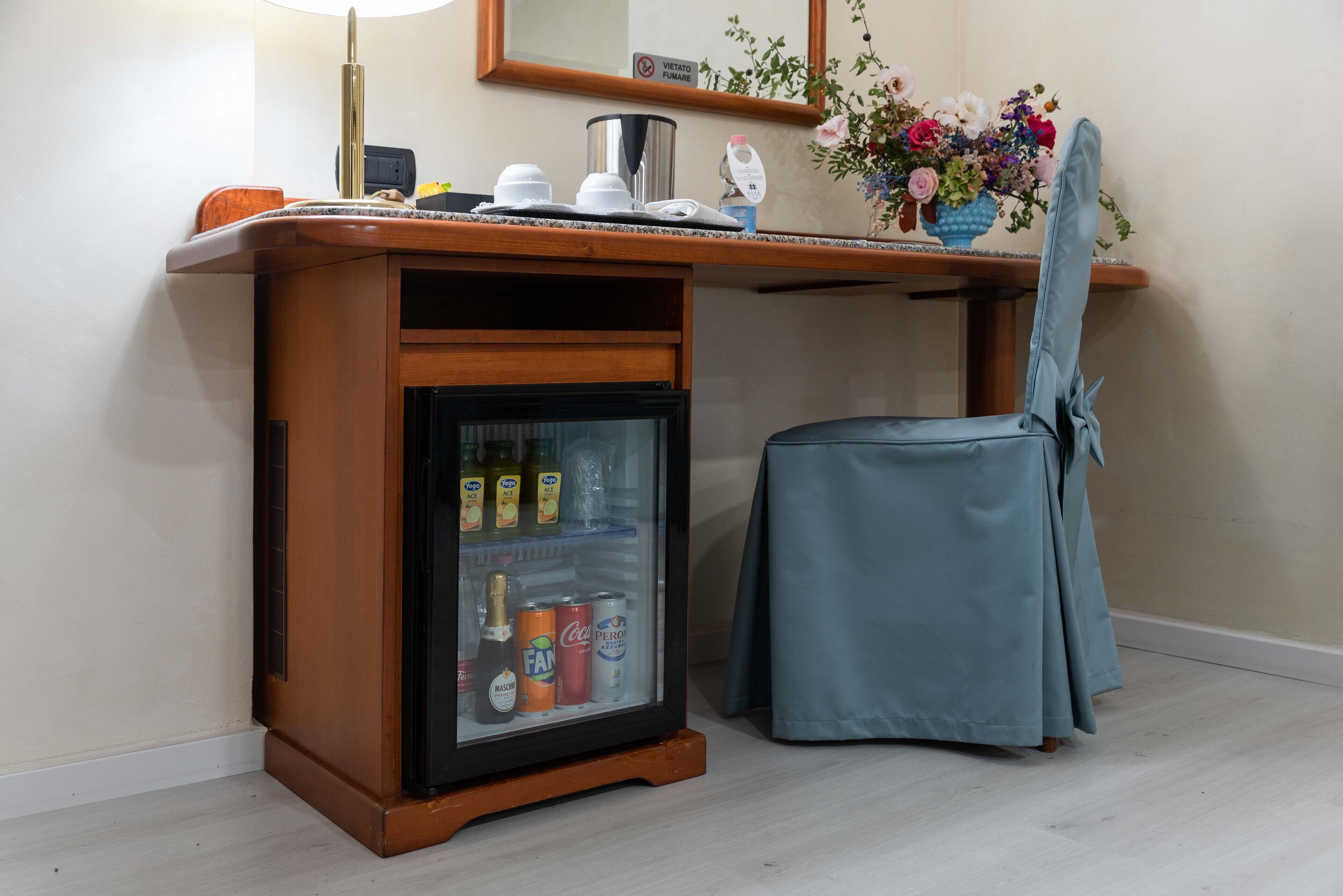 Eine Minibar mit einem Kühlschrank, der Getränke enthält, ein Sessel und ein kleiner Tisch mit Lampe und Blumenvase.