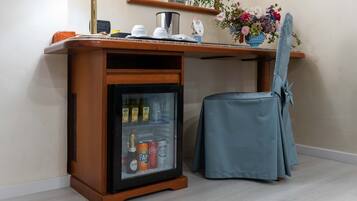 Eine Minibar mit einem Kühlschrank, der Getränke enthält, ein Sessel und ein kleiner Tisch mit Lampe und Blumenvase.
