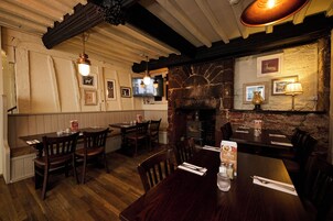 A restaurant with wooden tables and chairs, a stone fireplace, and a television mounted on the wall.
