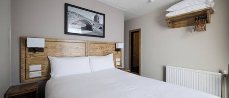 Una cama bien hecha con cabecera de madera, un cuadro colgado en la pared y un perchero encima.