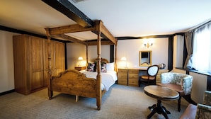 A four-poster bed with a wooden headboard, a wooden wardrobe, a desk with a mirror, and two upholstered chairs. - White Hart, Exeter by Marston's Inns (Exeter)