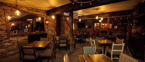A rustic bar with wooden furniture, stone walls, and hanging light fixtures.