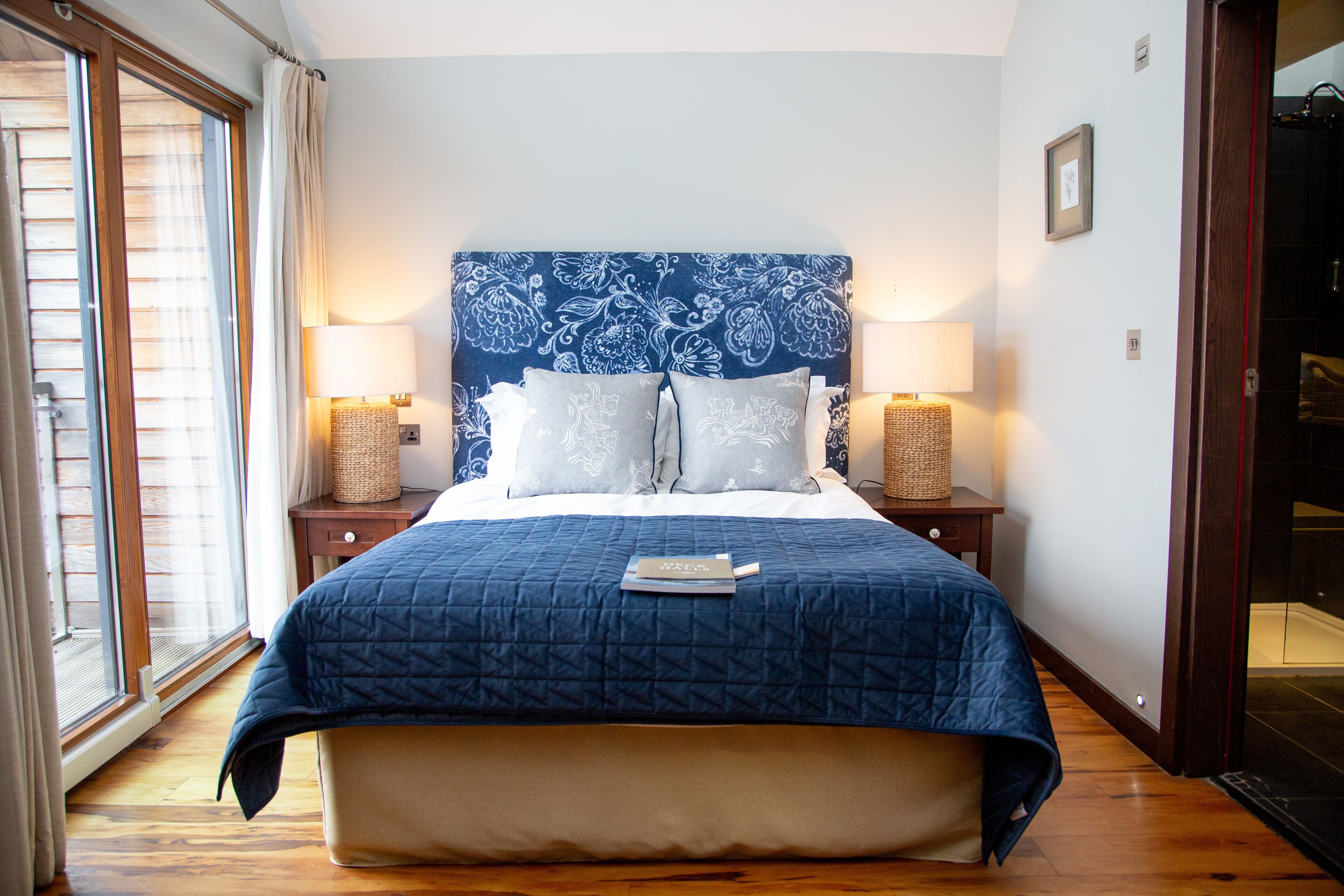 A bedroom with a large bed, two bedside tables, a window with curtains, and a door leading to a bathroom.