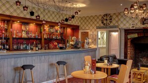 Eine Bar mit Hockern, ein runder Tisch mit Stühlen, eine Uhr und ein Kamin.