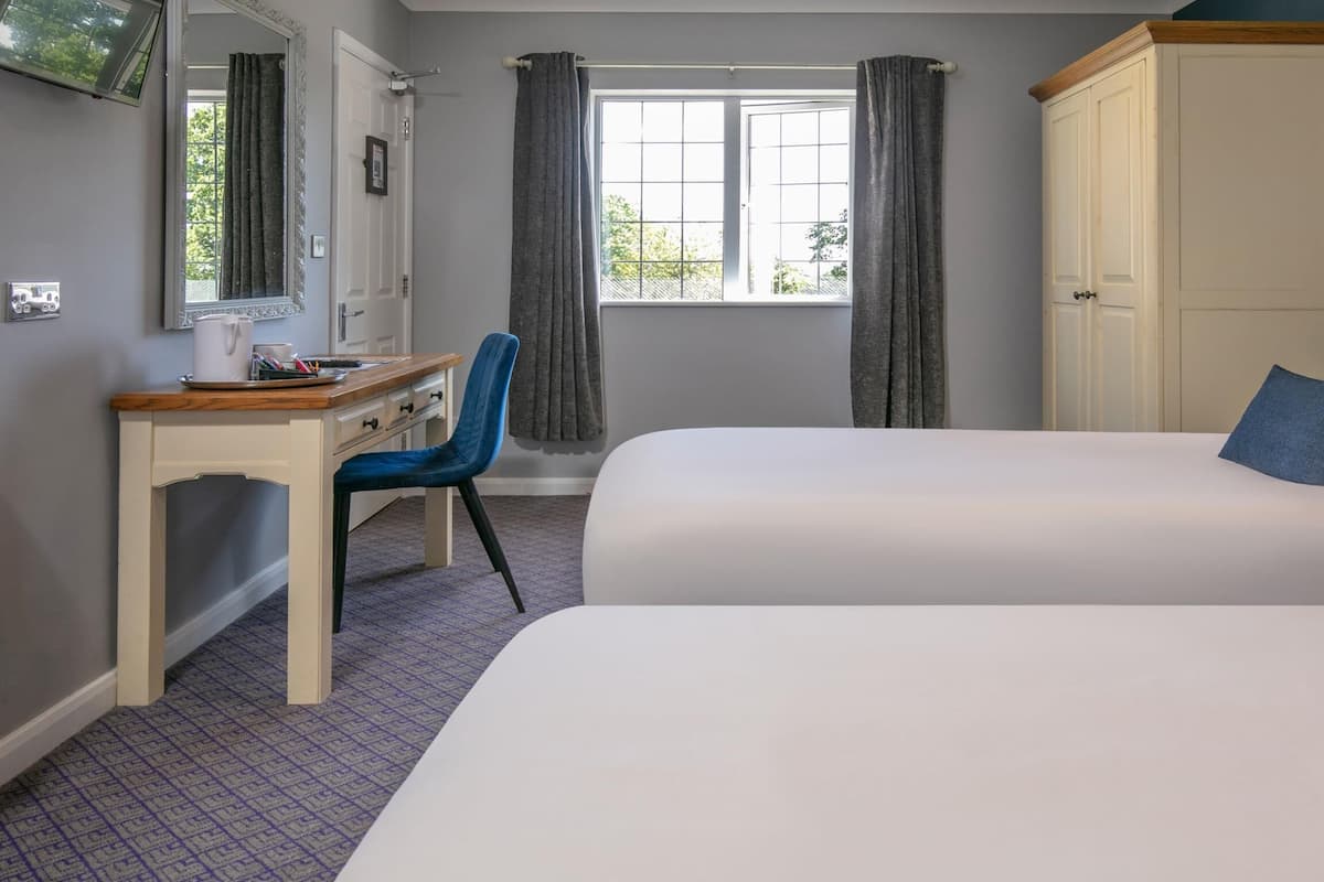 A bedroom with a bed, a desk, and a chair. There is a window with curtains, a wardrobe, and a television on the wall.