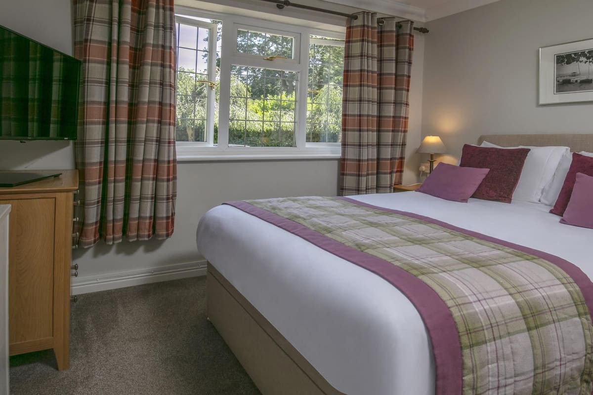 A bedroom with a bed, curtains, a bedside lamp, and a framed picture on the wall.
