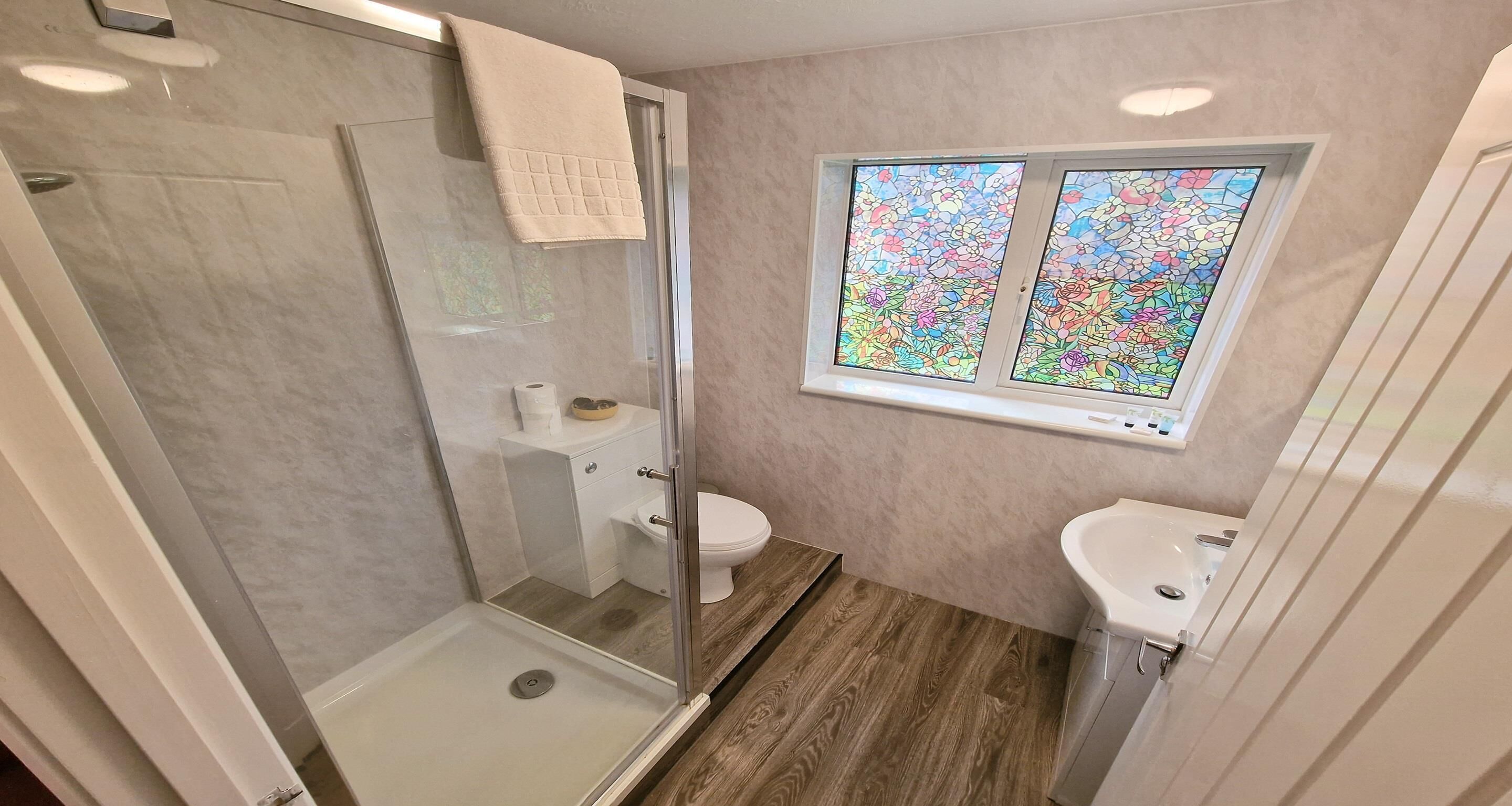 A bathroom with a glass shower enclosure, a toilet, a sink, and a stained glass window.