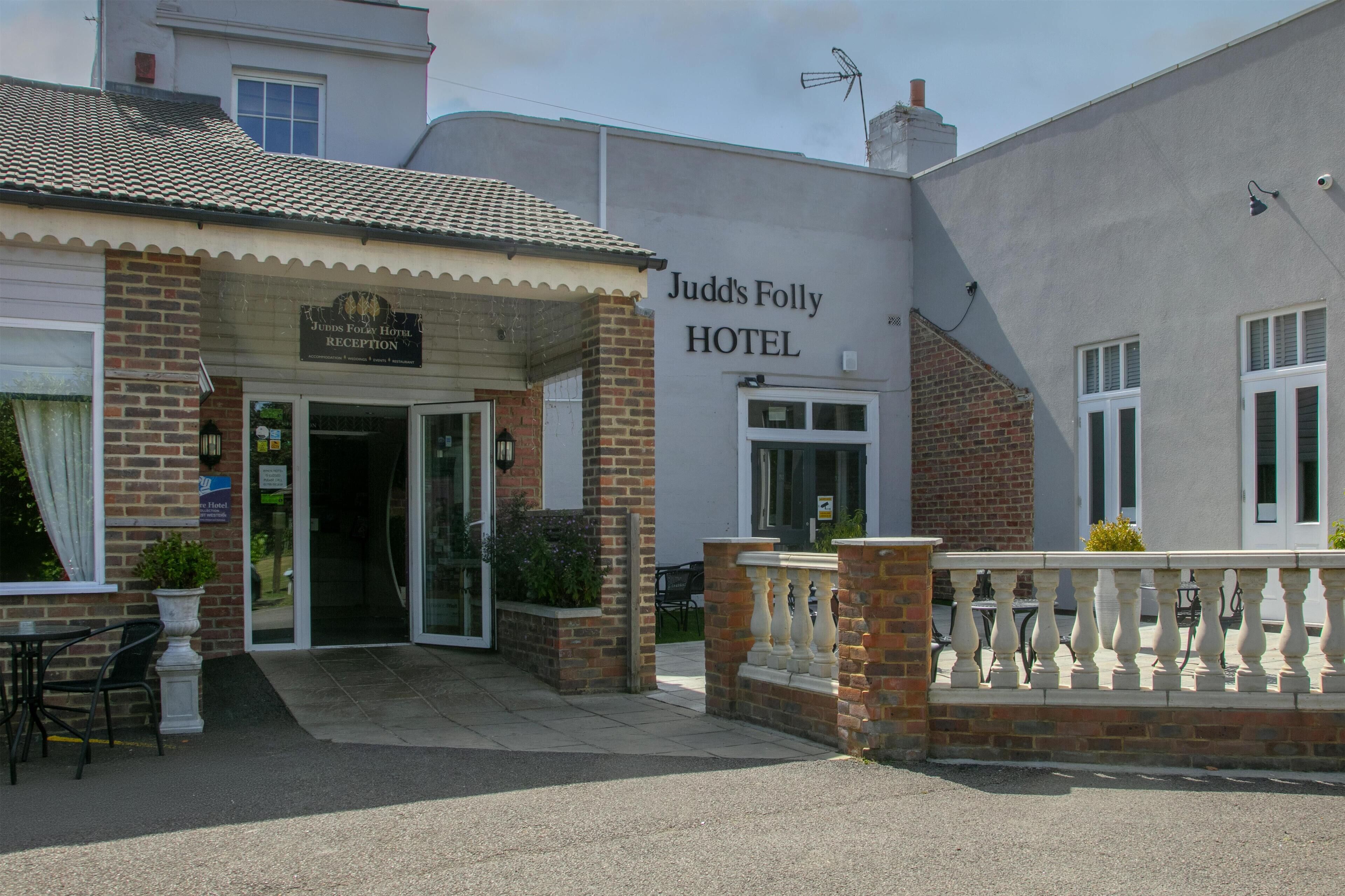The entrance of Judd's Folly Hotel with a reception area, outdoor seating, and a clear view of the hotel name on the facade.