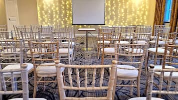 A conference room with rows of white chairs, a projector screen, and a carpeted floor.