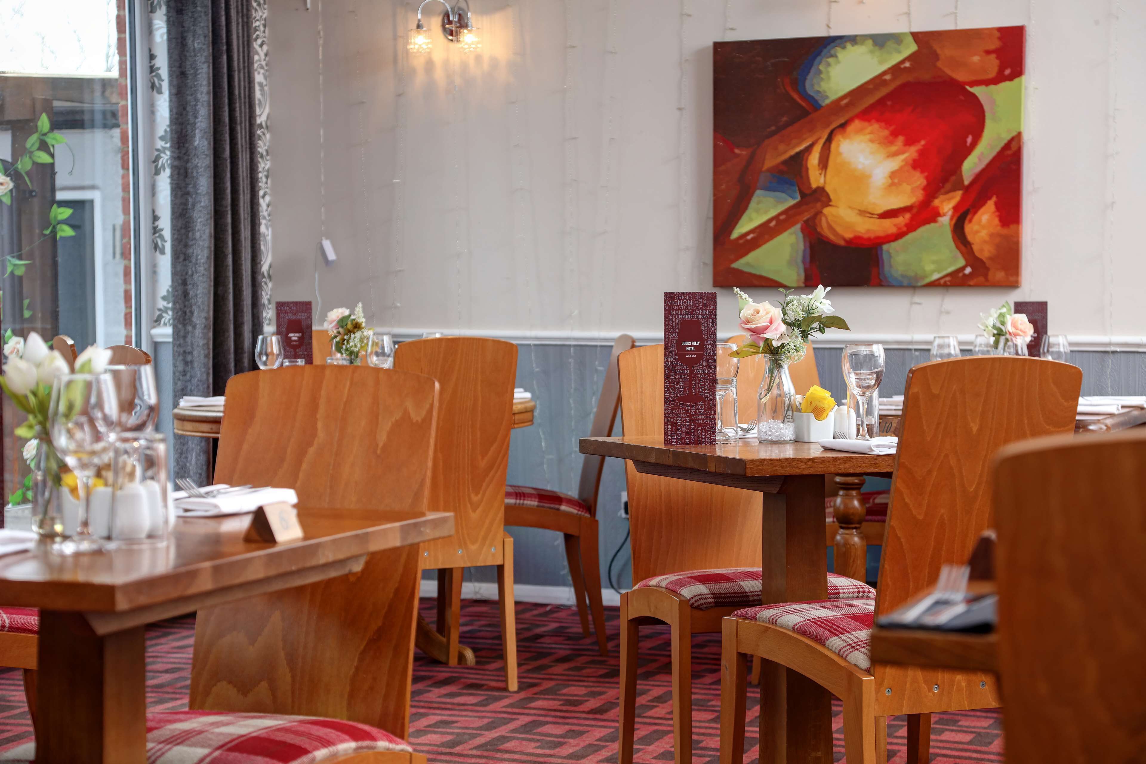 A restaurant with wooden tables and chairs, a menu stand, and a colorful painting on the wall.