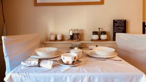 A dining table set with white tableware, a framed painting above, and a breakfast menu sign on the wall. - The Blue Cow (Huntingdon)