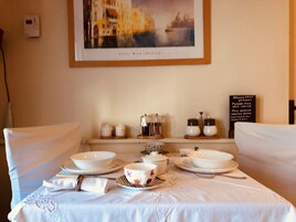 Una mesa de comedor dispuesta con vajilla blanca, un cuadro enmarcado encima y un cartel de menú de desayuno en la pared.