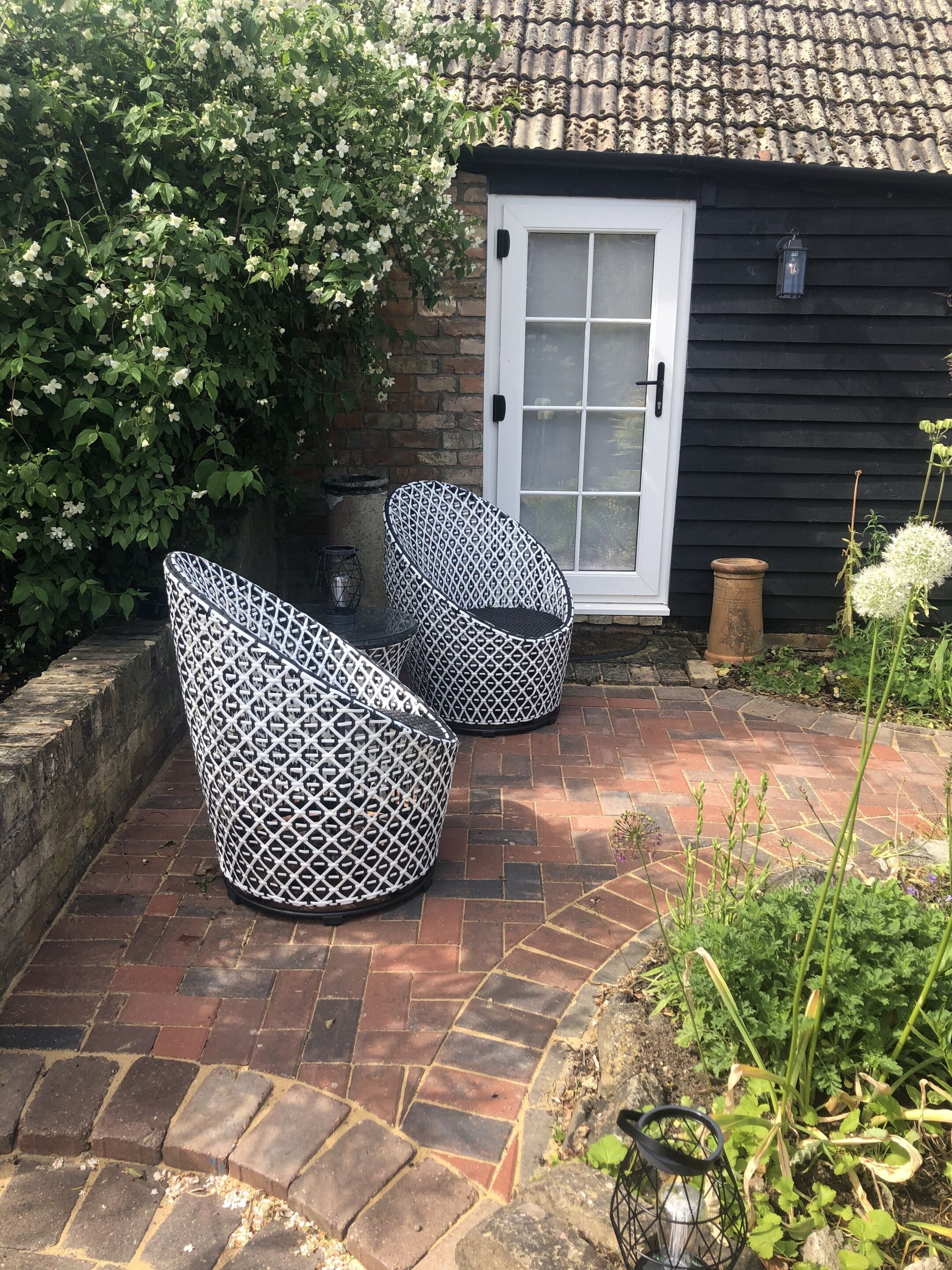 Outdoor seating with a patterned design, a brick pathway, and a building with a tiled roof and a white door.