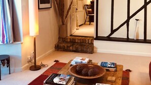 A cozy living room with a wooden coffee table, books, and decorative items. A staircase with a black railing leads to another room. - The Blue Cow (Huntingdon)