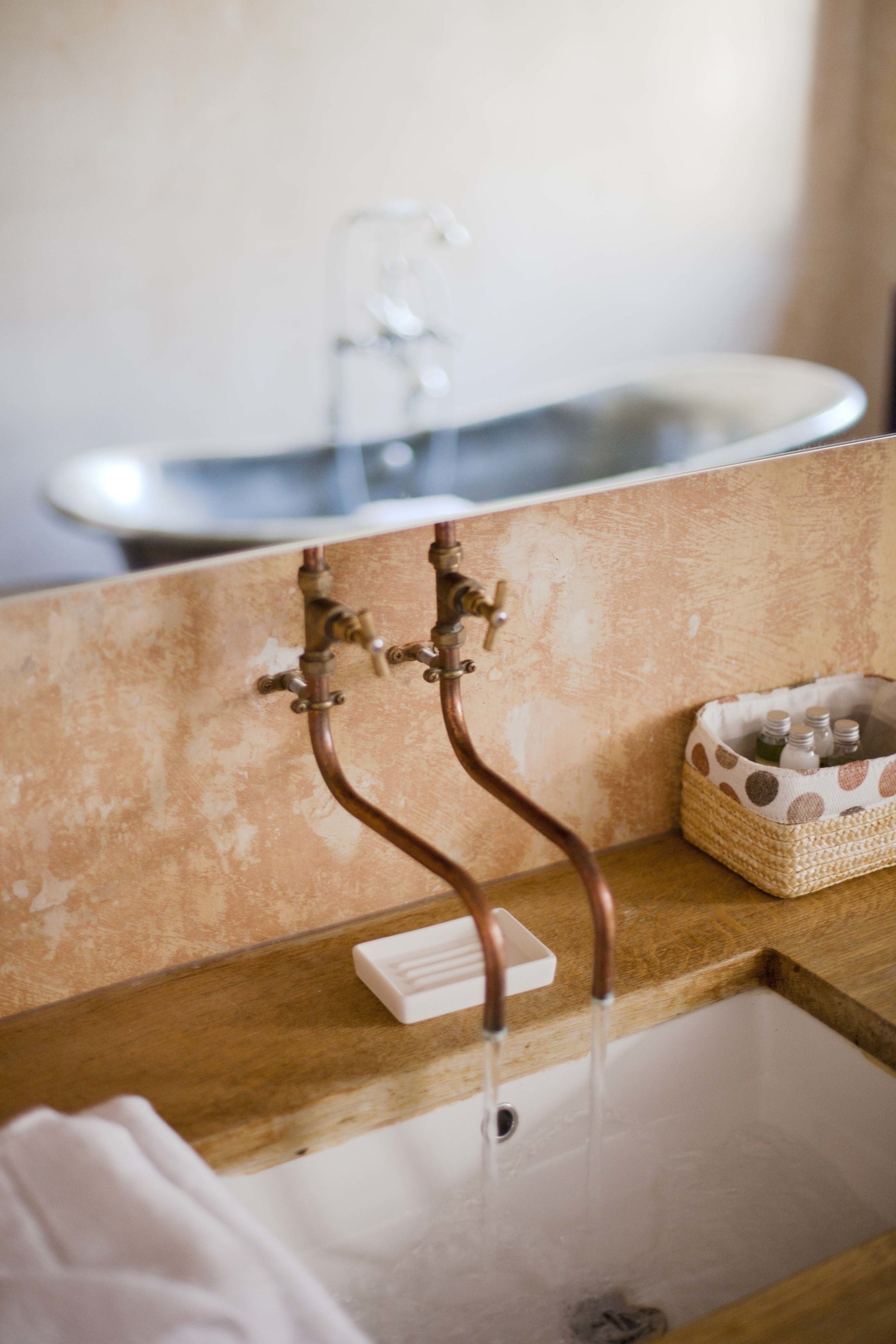 Une salle de bain avec un meuble-lavabo en bois, un lavabo blanc et un petit panier tressé contenant des bouteilles.