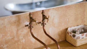 Une salle de bain avec un meuble-lavabo en bois, un lavabo blanc et un petit panier tressé contenant des bouteilles.