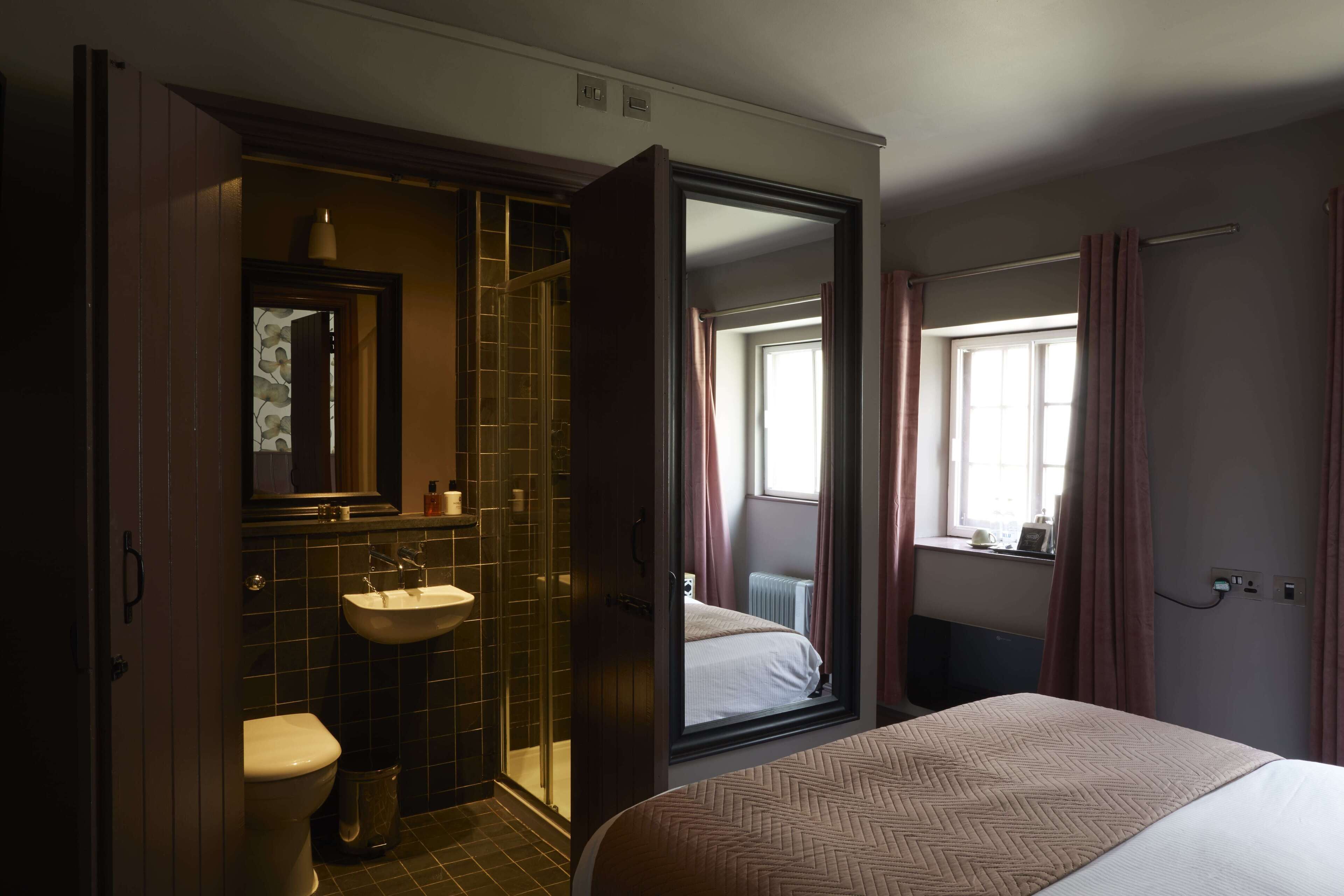 Habitación de hotel con cama, baño con lavabo e inodoro, y un espejo grande.