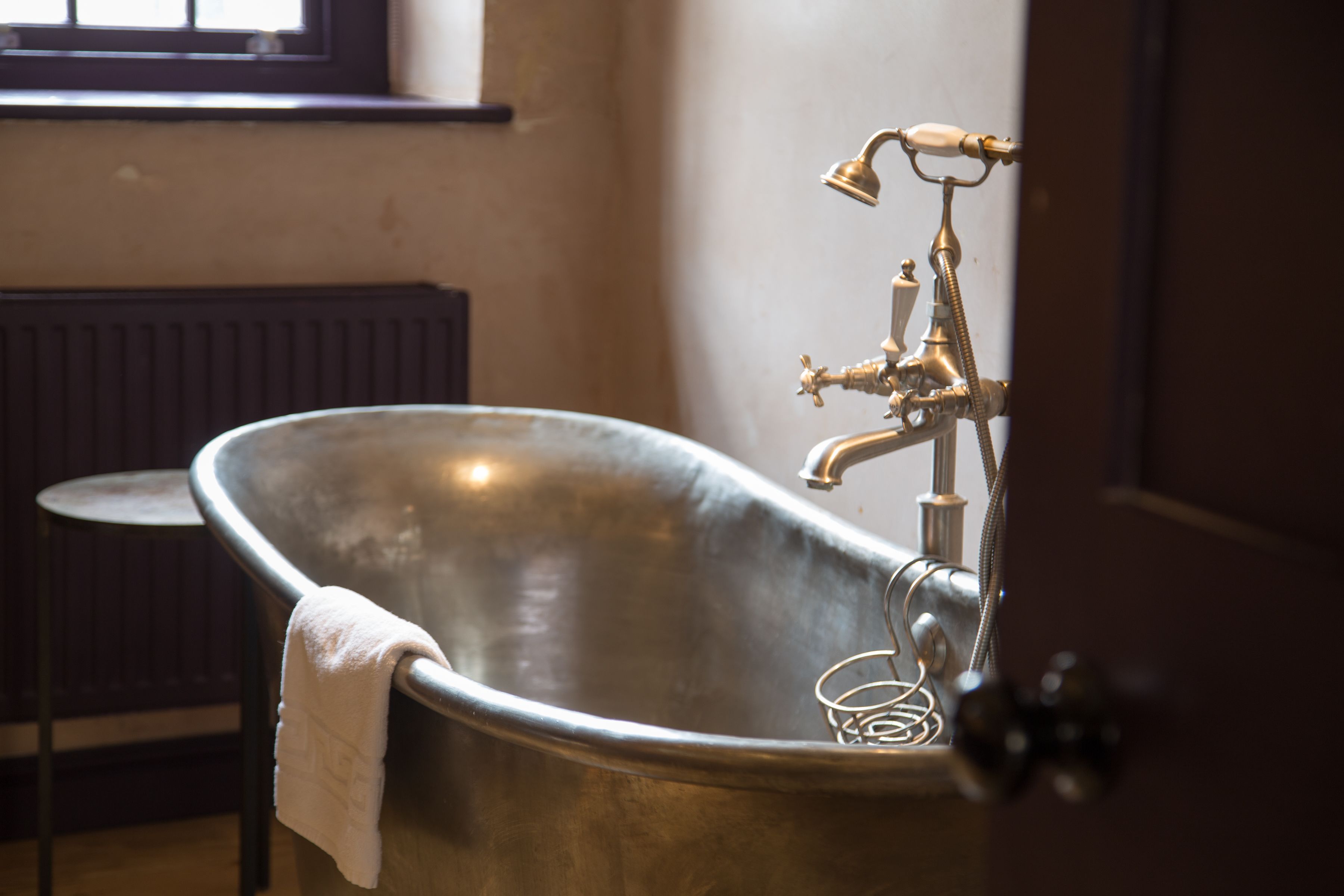 Une baignoire de style rétro, avec une serviette suspendue sur le bord, un radiateur en arrière-plan et une fenêtre au-dessus de la baignoire.