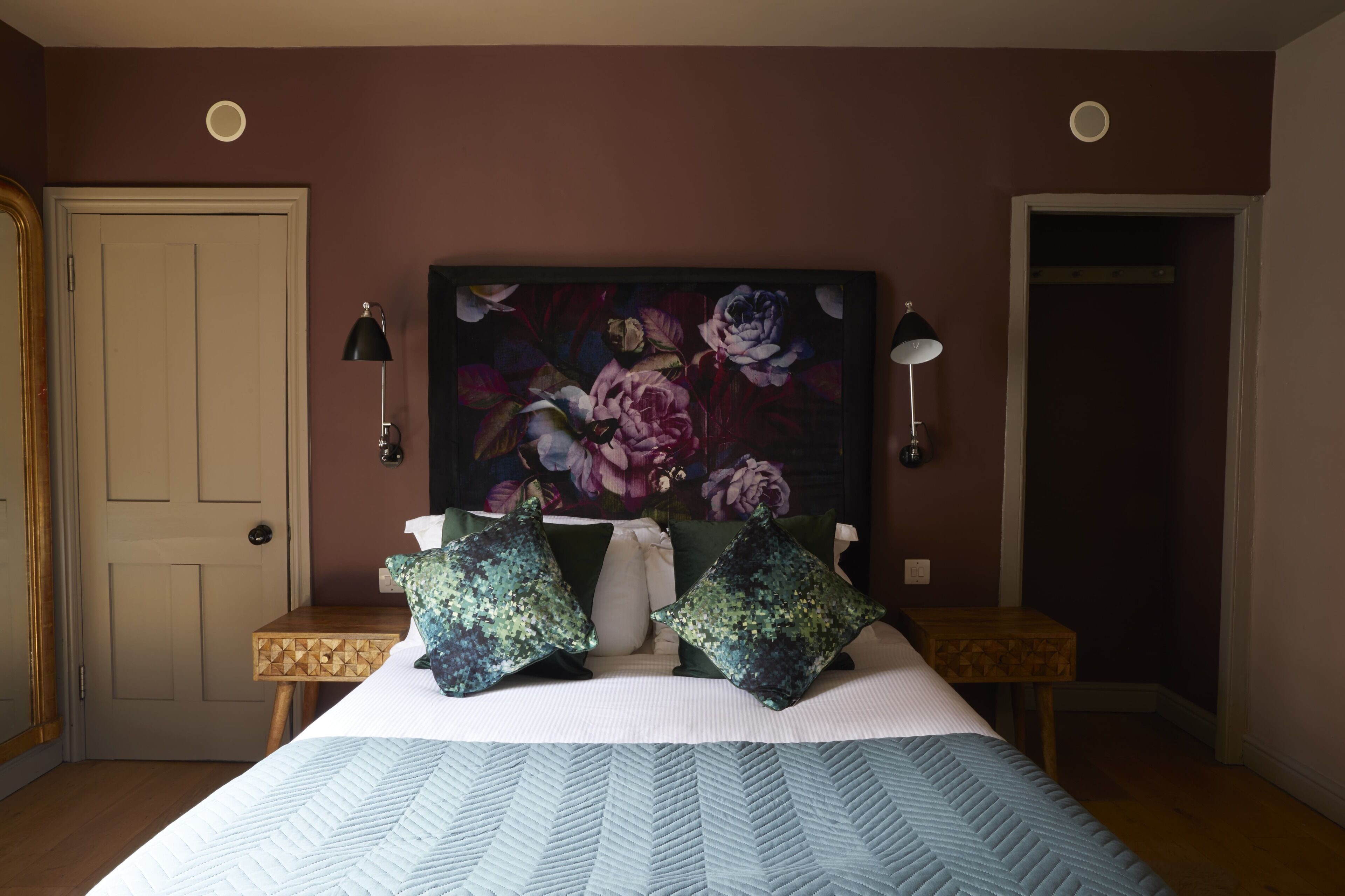 Une chambre à coucher avec un grand lit, deux tables de chevet, un tableau au mur et une porte.