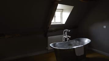 Un dormitorio abuhardillado con poca luz, techo inclinado, un ventanal grande y una bañera independiente.