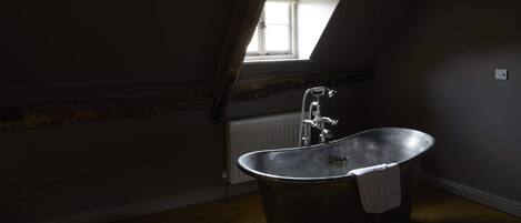 Une chambre mansardée à l’éclairage tamisé, avec un plafond en pente, une grande fenêtre et une baignoire sur pieds.