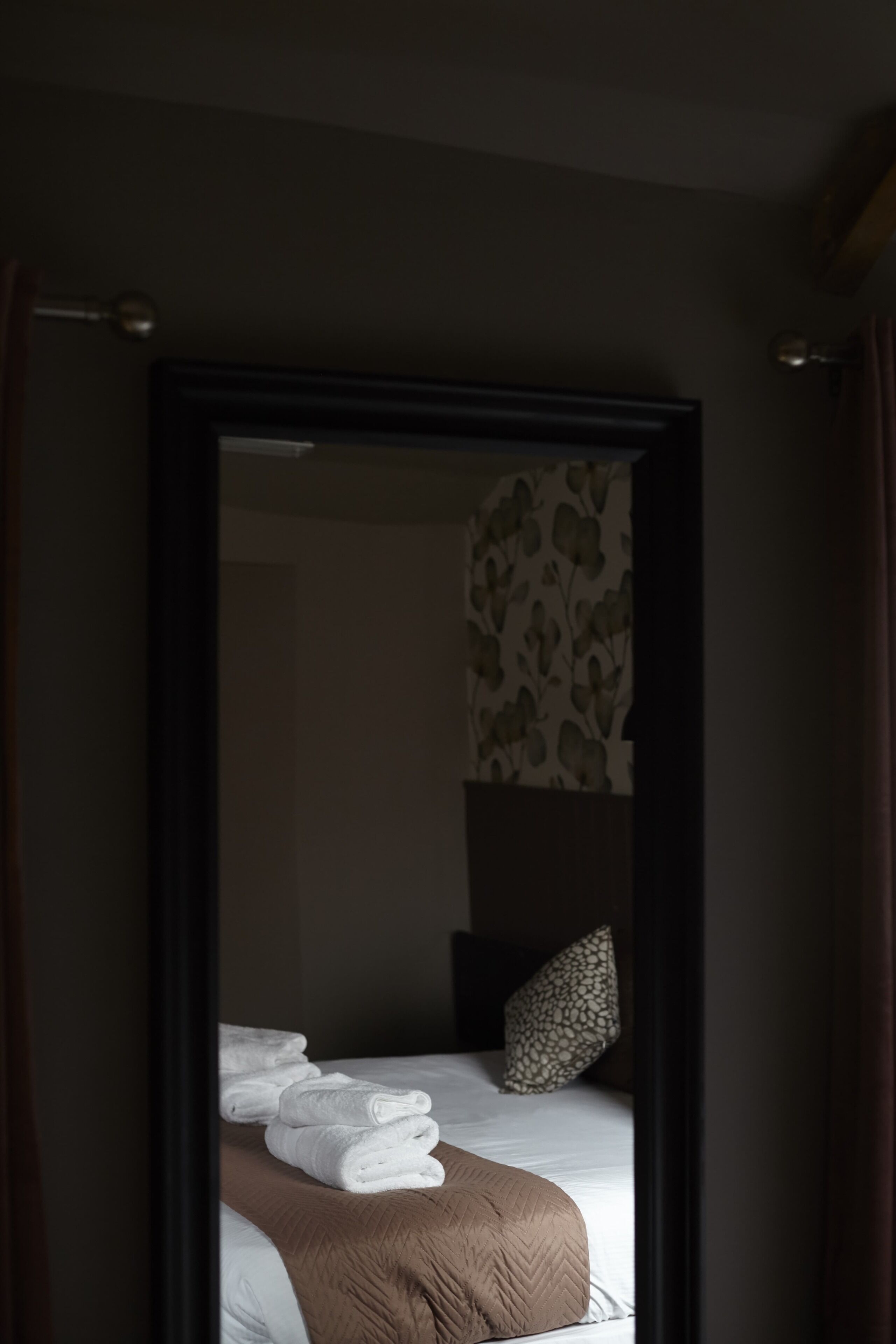 A hotel room with a bed, white towels, a brown blanket, and a patterned pillow.