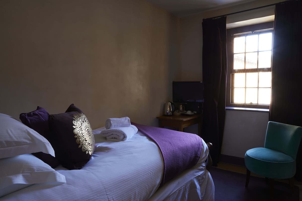 A hotel room with a bed, a chair, a television, and a window with curtains.