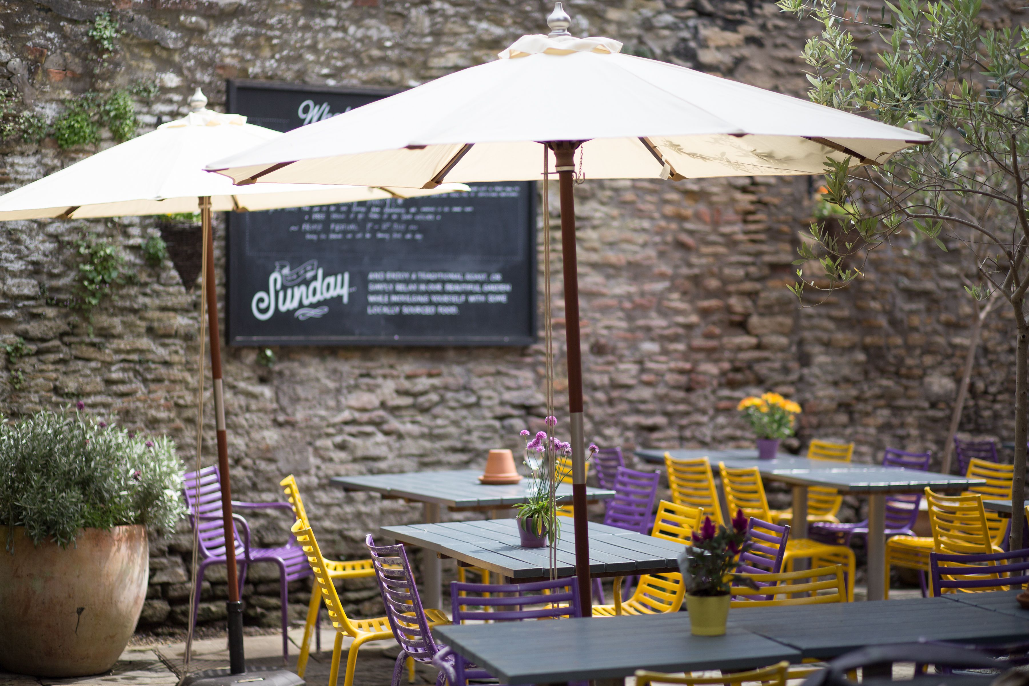 Un espace extérieur aménagé avec des tables et des chaises, un mur en pierre et un panneau affichant le menu.