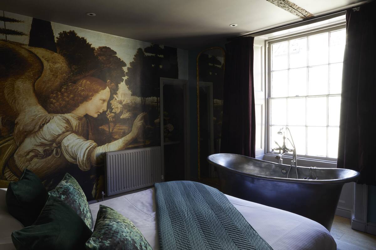 A bedroom with a large mural, a bathtub, and a window with curtains.