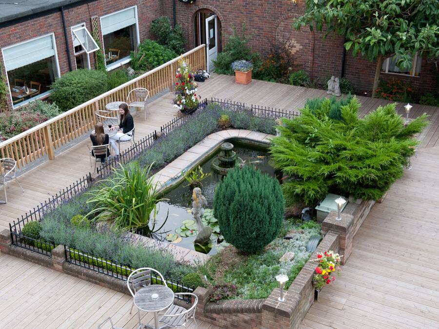 A rooftop garden with a pond, seating area, and potted plants.