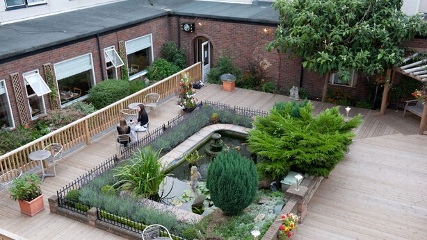 A courtyard with a wooden deck, seating areas, a small pond, and various plants. - King Charles Hotel (Gillingham)