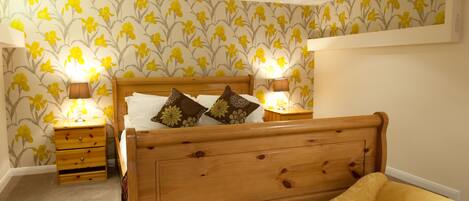 A bedroom with a wooden bed, two bedside tables with lamps, a nightstand, and floral wallpaper.