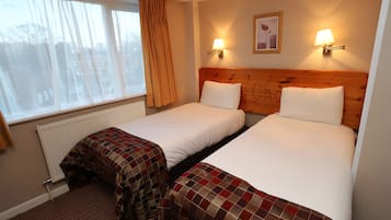 Una habitación de hotel con dos camas, una ventana con cortinas, un radiador y dos lámparas fijadas a la pared.