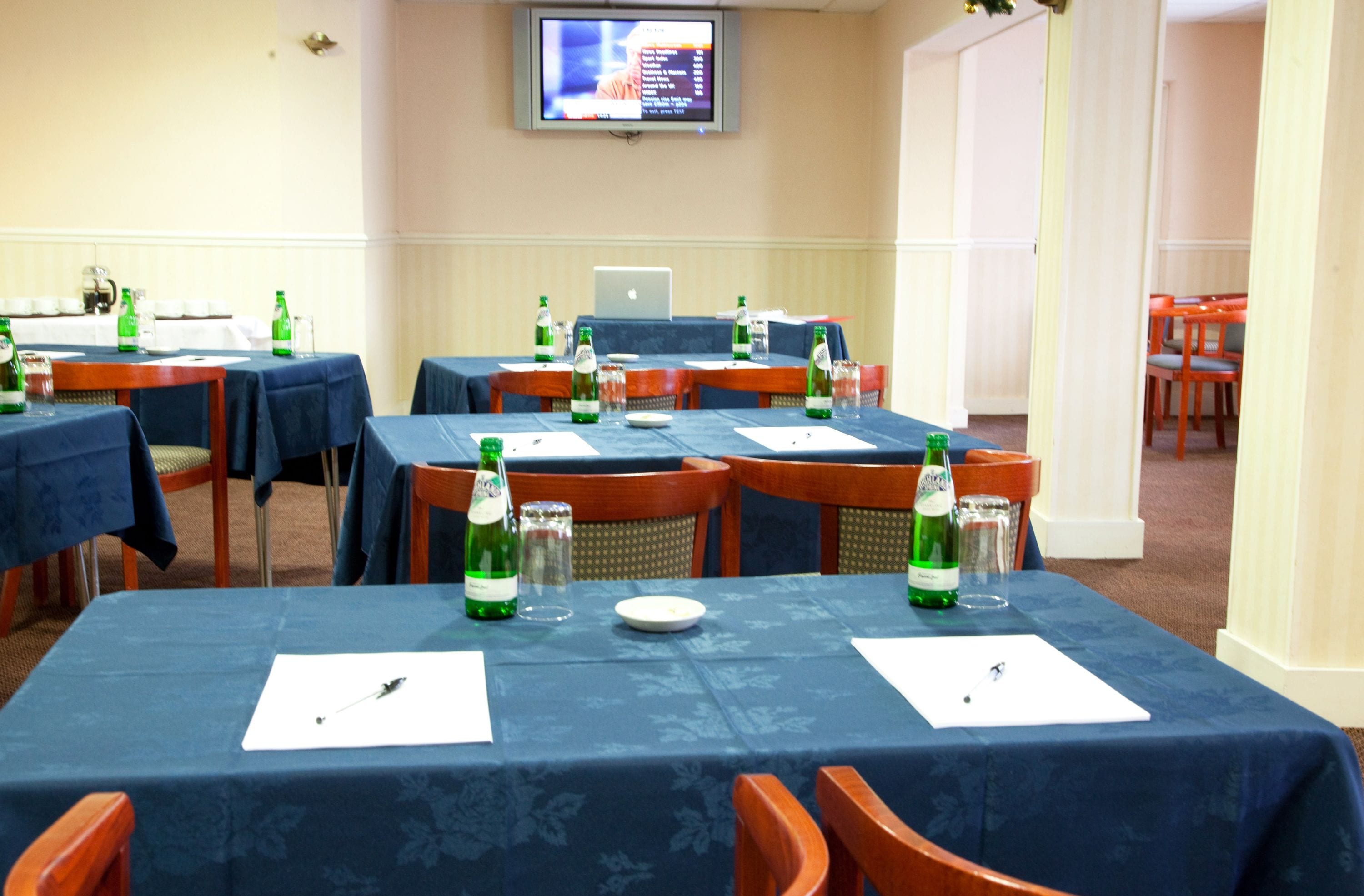 Un salón de conferencias con mesas dispuestas para reuniones, equipado con computadoras portátiles, documentos y bebidas.