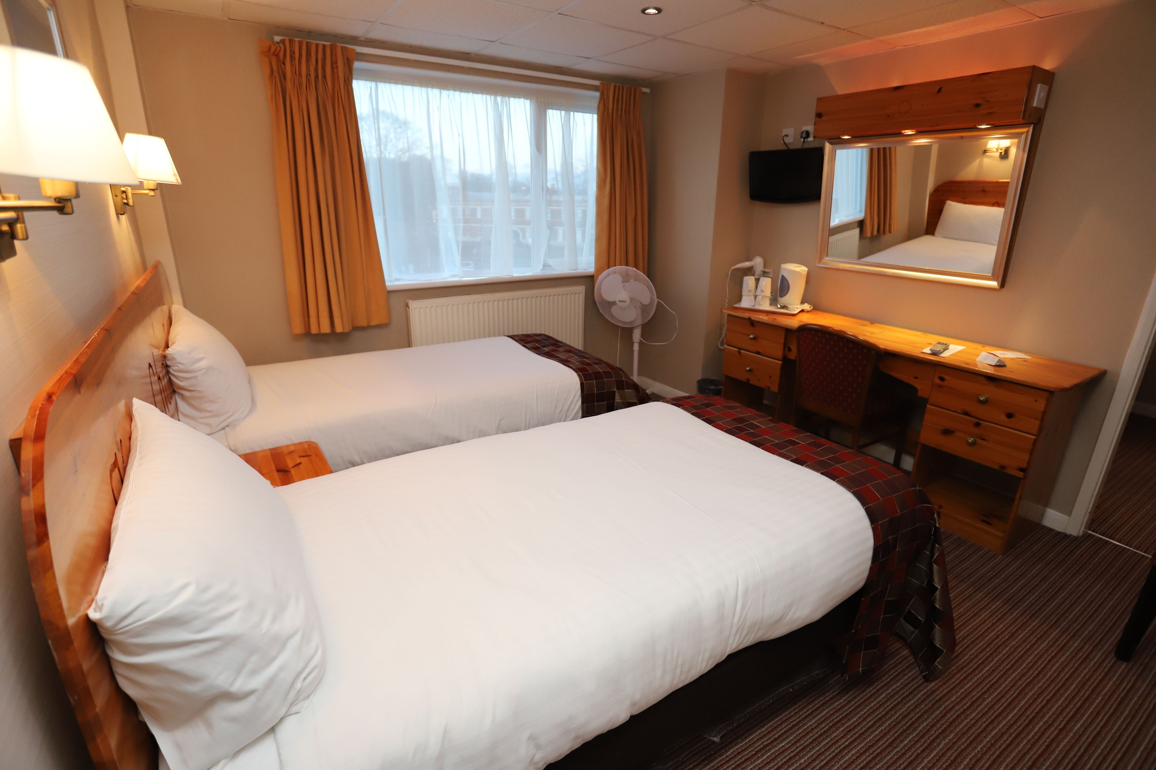 A hotel room with two beds, a desk, a mirror, and a window with curtains.