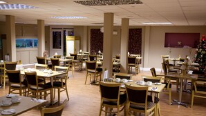 A spacious dining area with multiple tables and chairs, a Christmas tree, and a fish tank in the background. - King Charles Hotel (Gillingham)