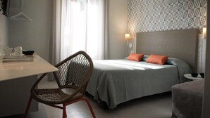 A hotel room with a bed, a desk, a chair, and a patterned wall.
