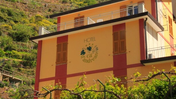 A hotel building with a balcony, a sign indicating it's a hotel, and a logo with a plant.