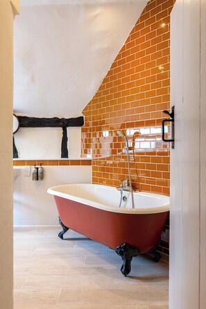 A modern bathroom with a freestanding bathtub, a tiled wall, and a wooden floor. - The Richard Onslow (Cranleigh)