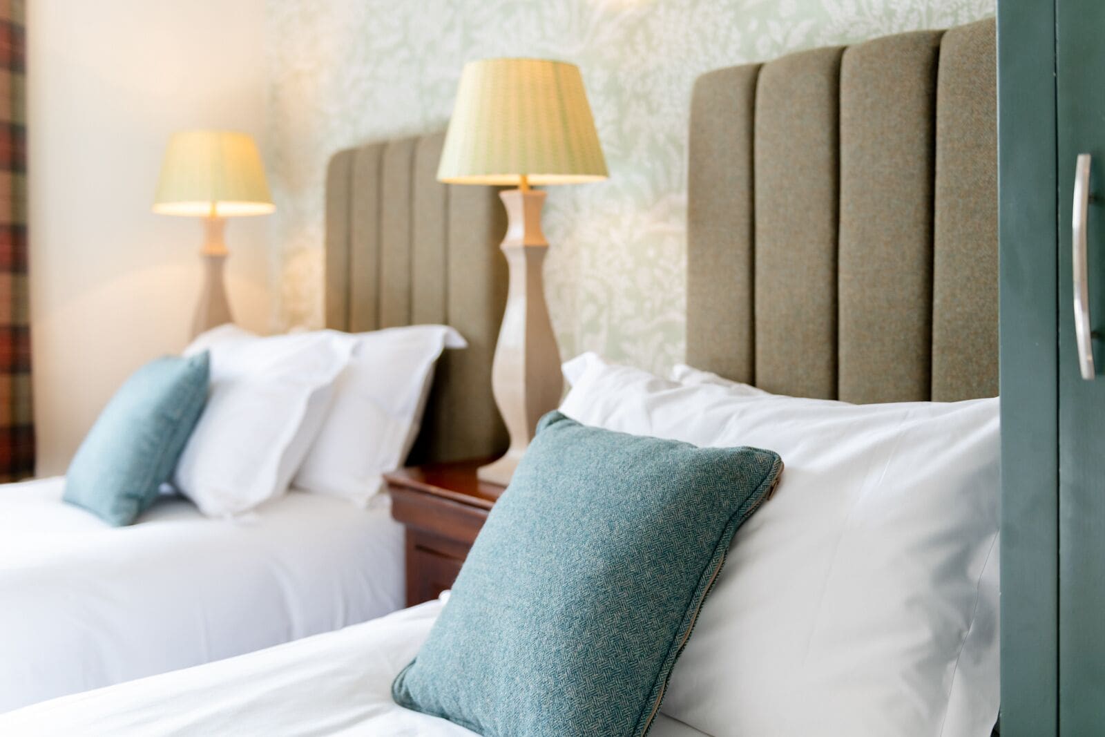 Une chambre d’hôtel avec deux lits, chacun doté d’une tête de lit, de draps blancs et d’une lampe sur une table de chevet.