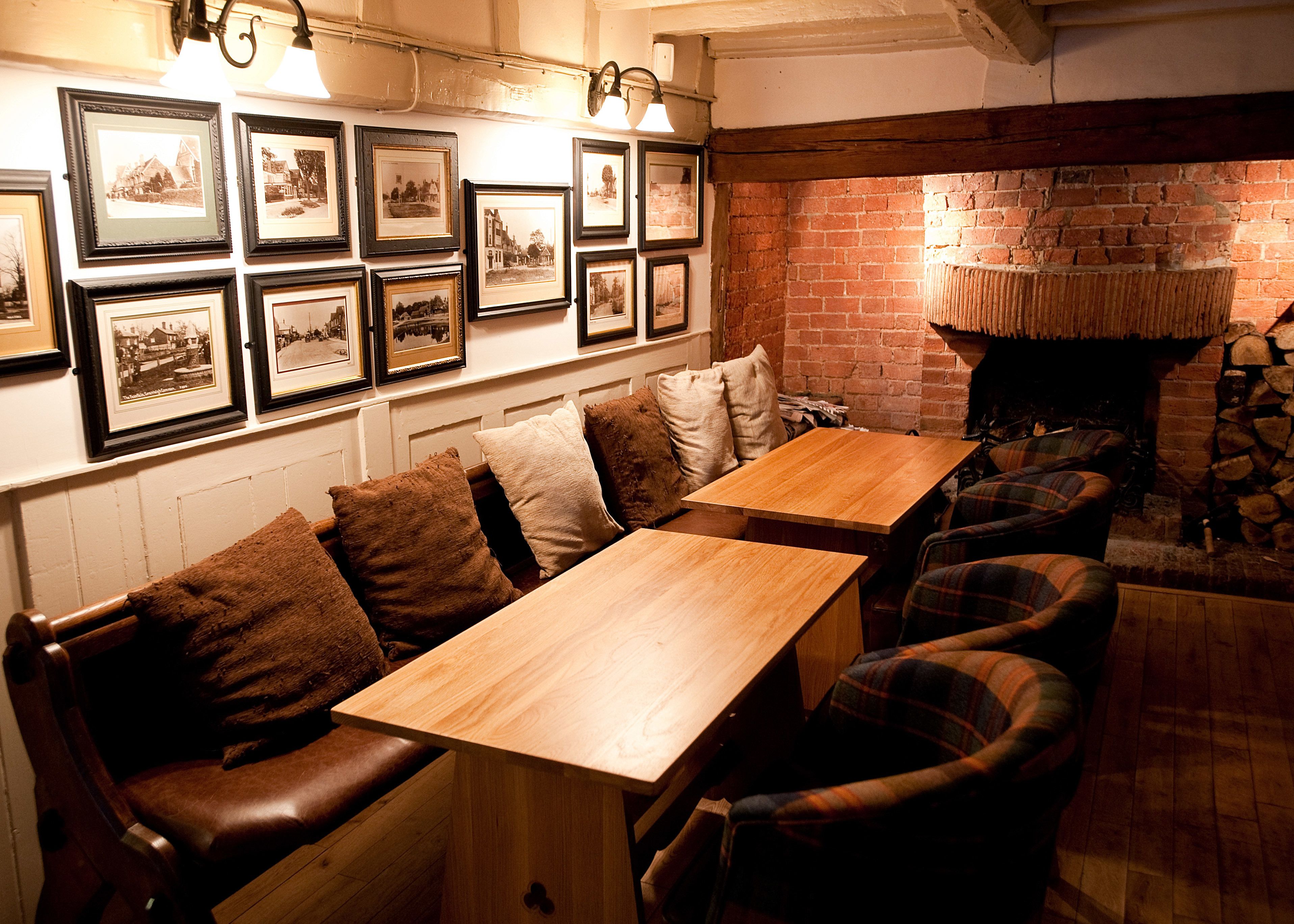 A cozy restaurant with wooden tables and benches, a brick fireplace, and framed pictures on the wall.