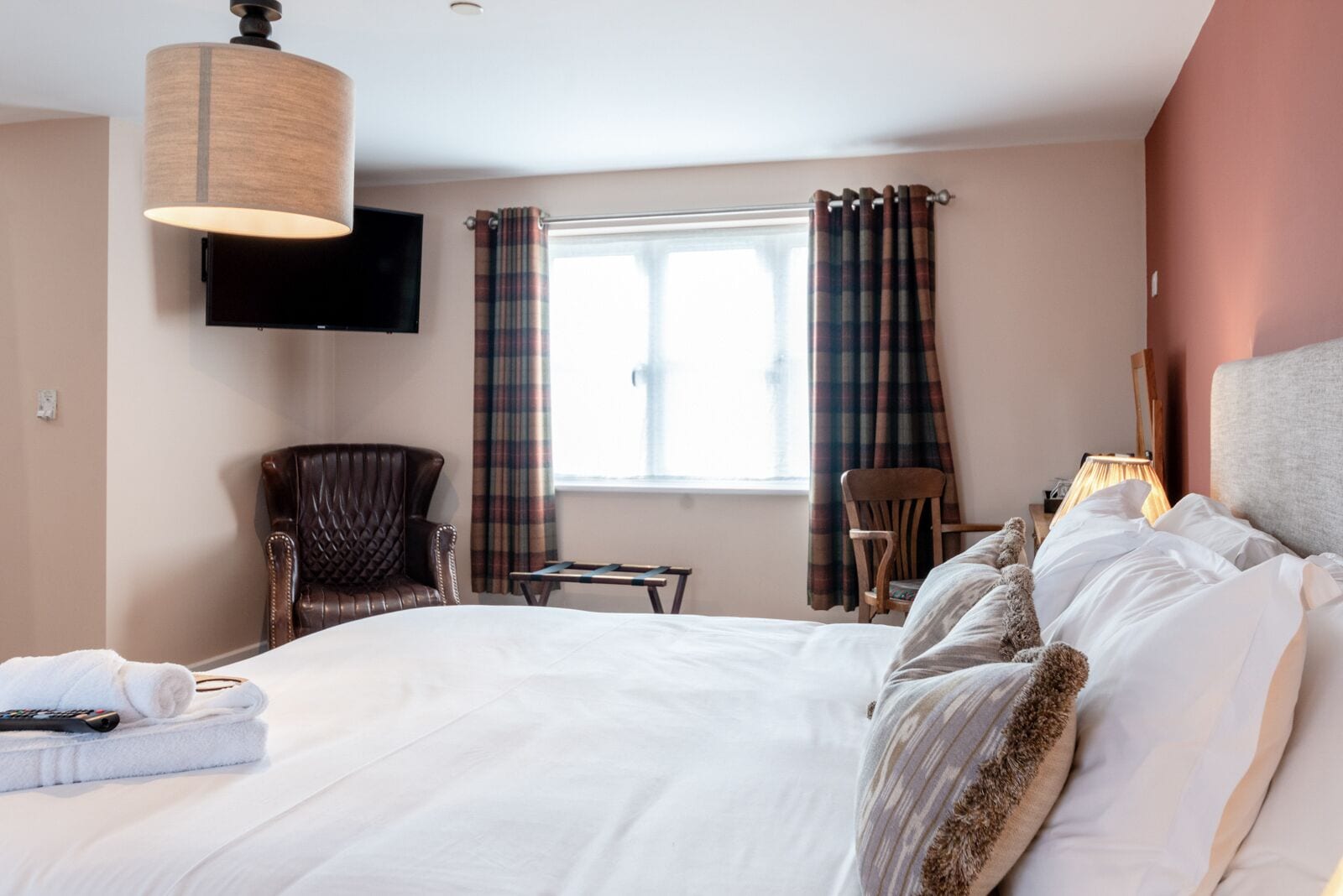 A hotel room with a large bed, two chairs, a television, and a window with curtains.